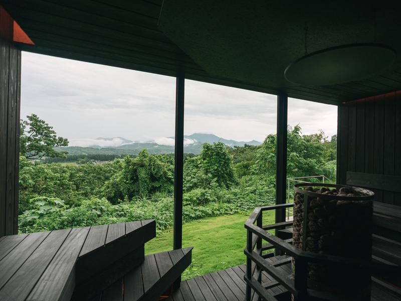 Snow Peak FIELD SUITE SPA HEADQUARTERS ３６０度型サウナヒーター。まるで焚火を囲んでいるような体験。一面ガラス張りで粟ヶ岳を一望出来る。サウナヒーターはMETOS社製のiki。冬季は雪景色をお楽しみいただけます。
